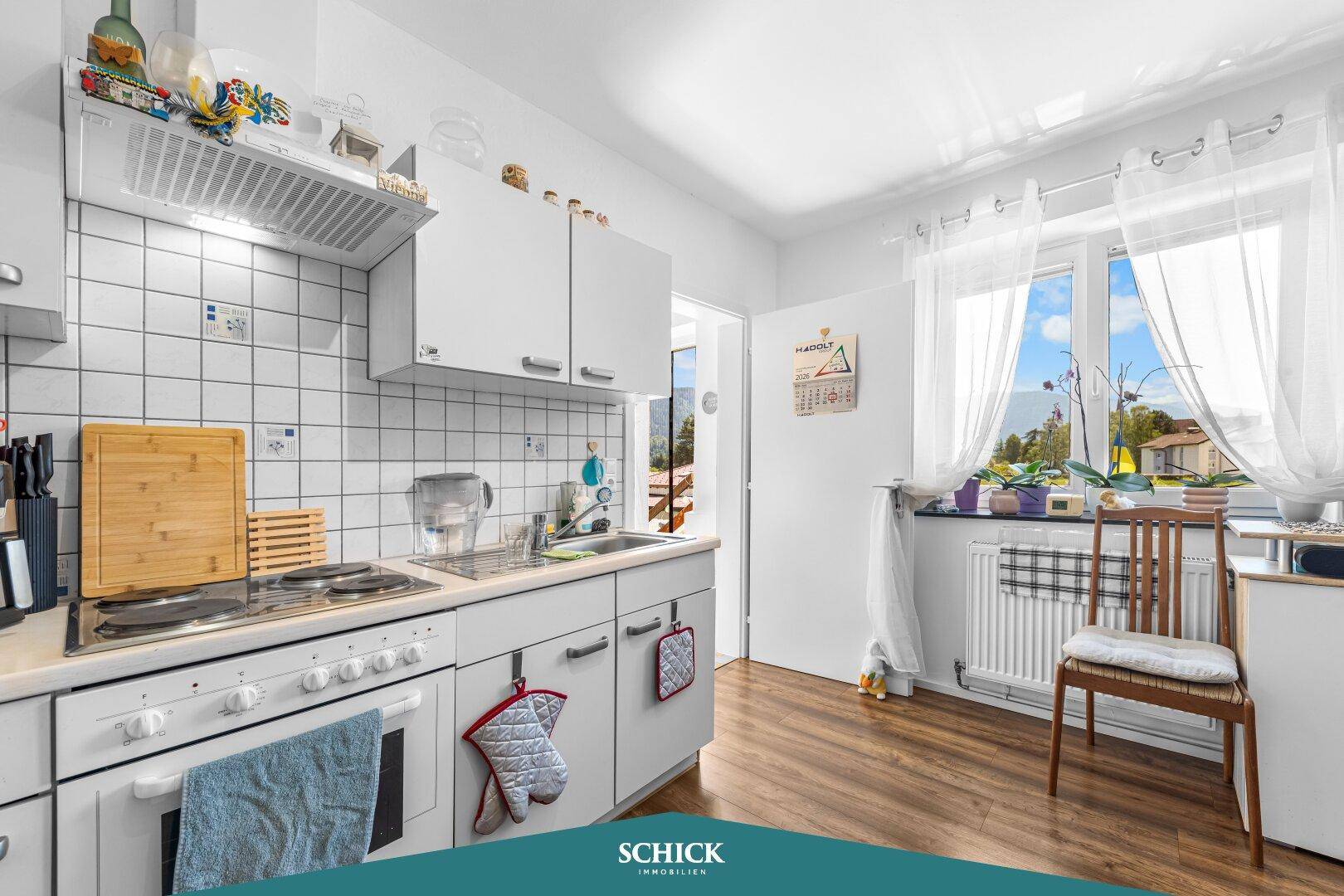 Helle Küche mit weißen Schränken, Fliesenrückwand und Fenster mit Ausblick.