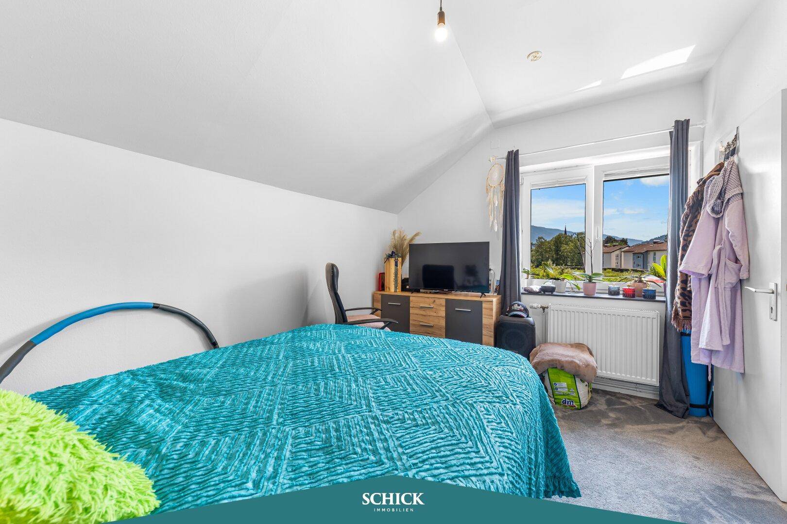 Gemütliches Schlafzimmer im Dachgeschoss mit schrägen Wänden, Fenster und Blick ins Grüne.