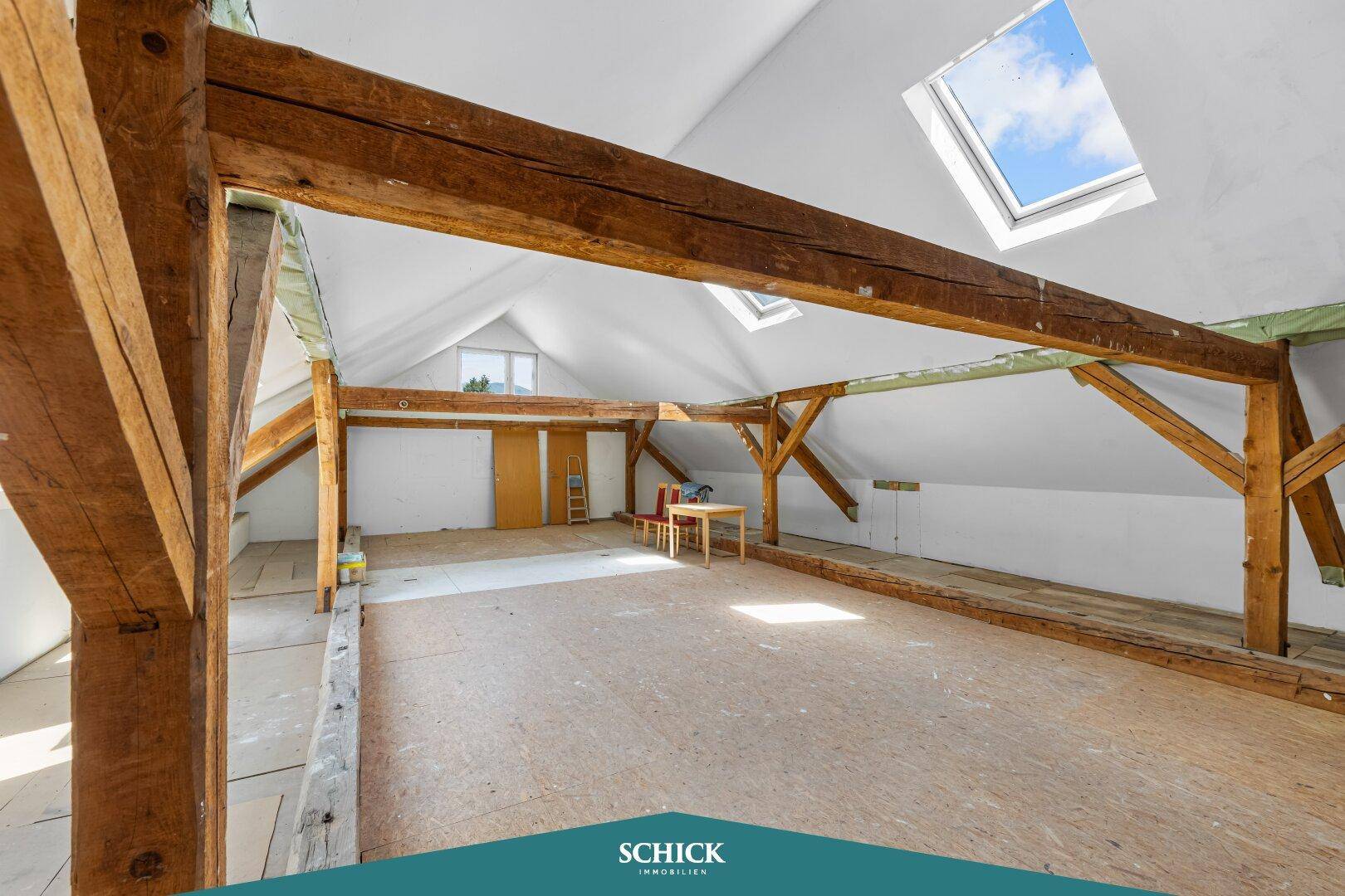 Geräumiger Dachboden mit sichtbaren Holzbalken, Dachschrägen und Dachfenstern.