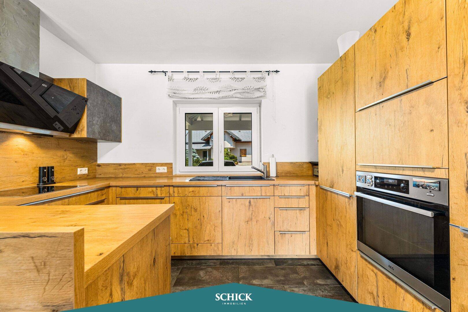 Moderne Küche mit Holzfronten, integriertem Backofen und Fenster mit Blick ins Grüne.