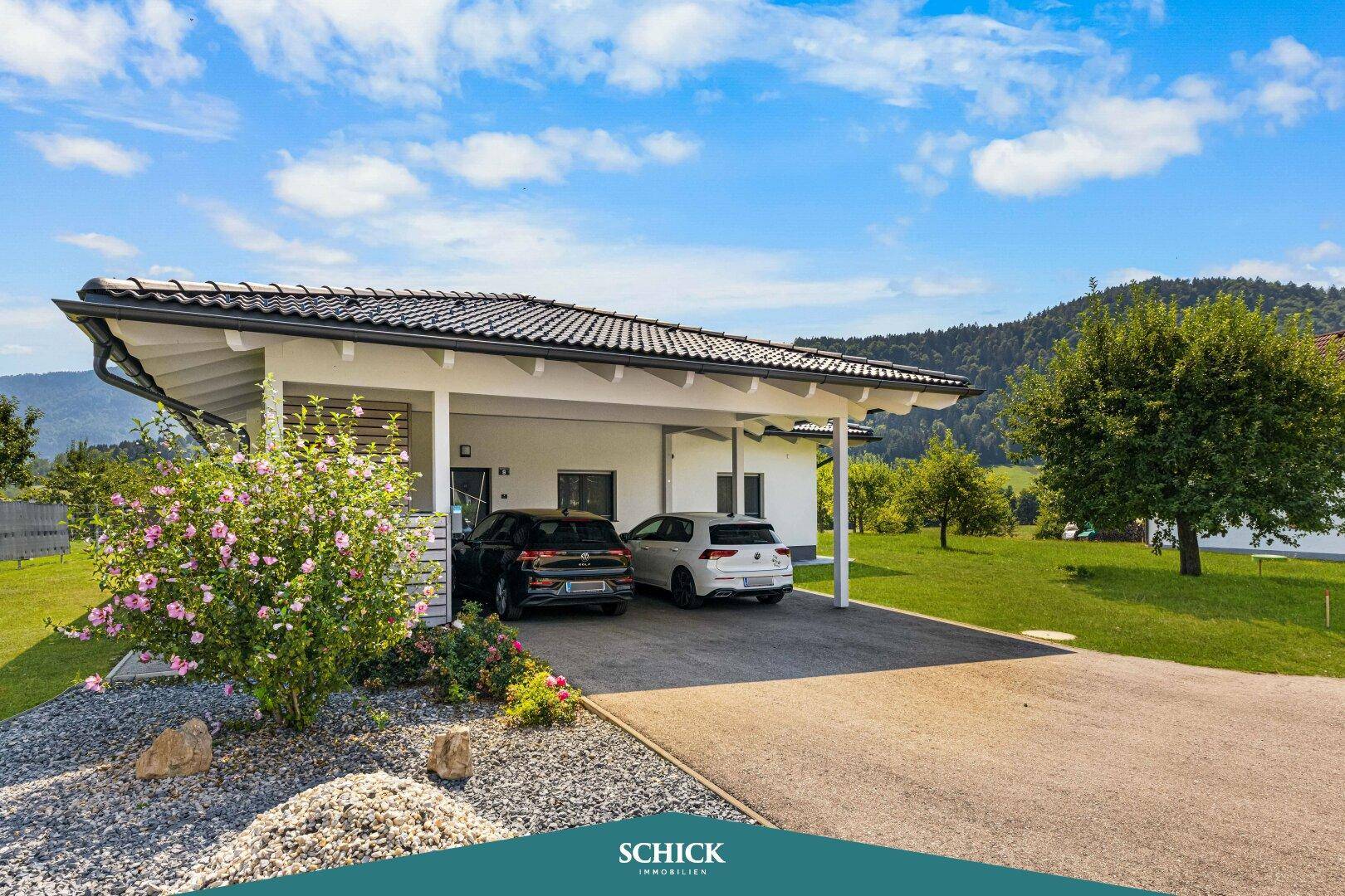 Ansicht des Hauses mit Carport für zwei Fahrzeuge und blühenden Sträuchern im Vorgarten.