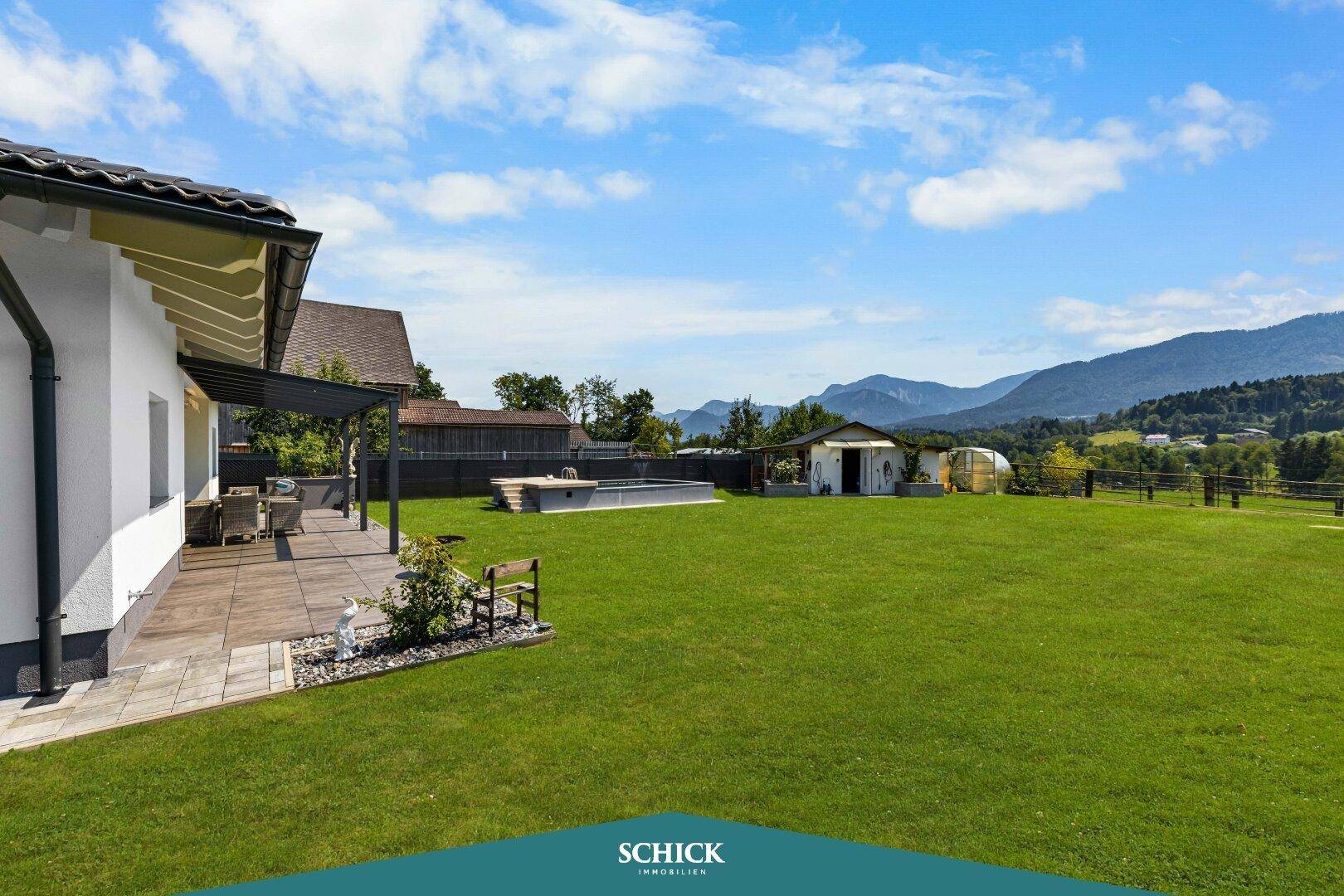 Weitläufiger Garten mit Rasenfläche, Terrasse und malerischem Blick auf die umliegenden Berge.