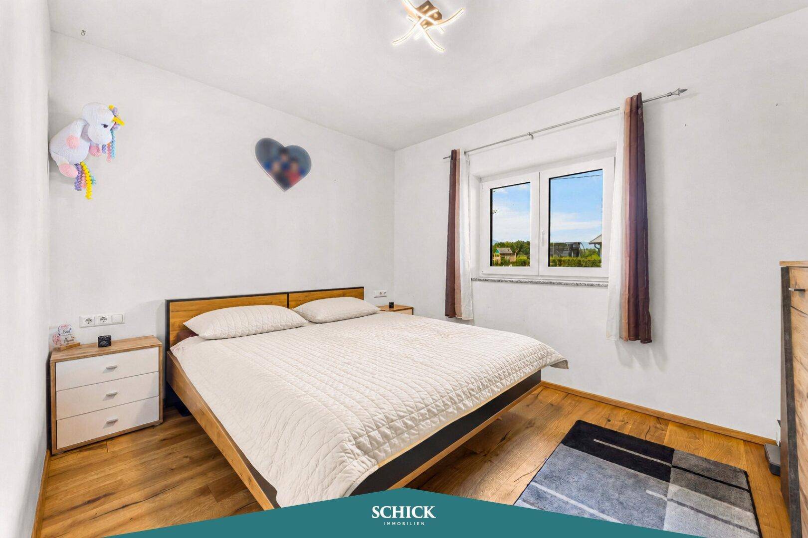 Helles Schlafzimmer mit Holzbett, Nachttischen und Fenster mit Blick ins Grüne.