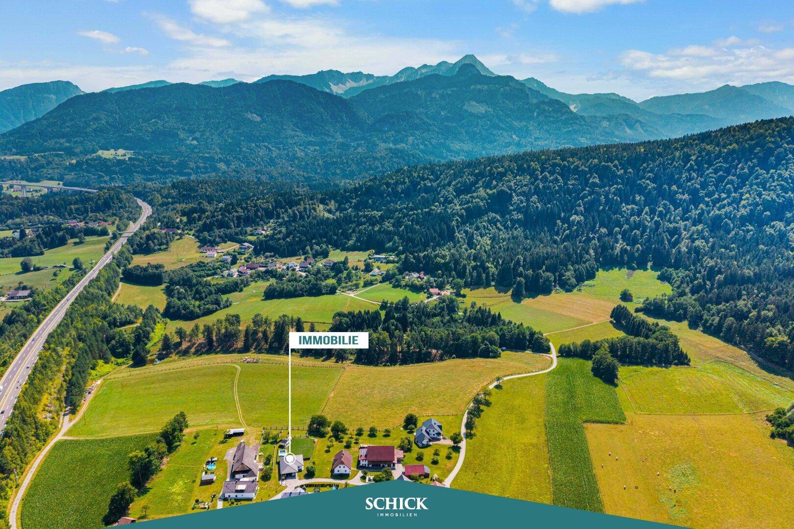 Panoramablick aus der Vogelperspektive auf eine ländliche Gegend mit weiten Feldern und majestätischen Bergen im Hintergrund.