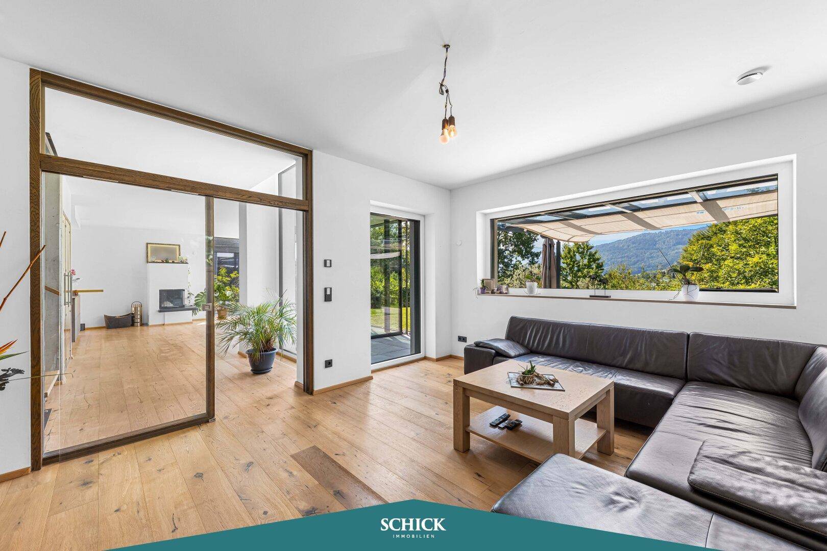 Gemütliches Wohnzimmer mit Ledersofa, Holzboden und großem Fenster mit Gartenblick.