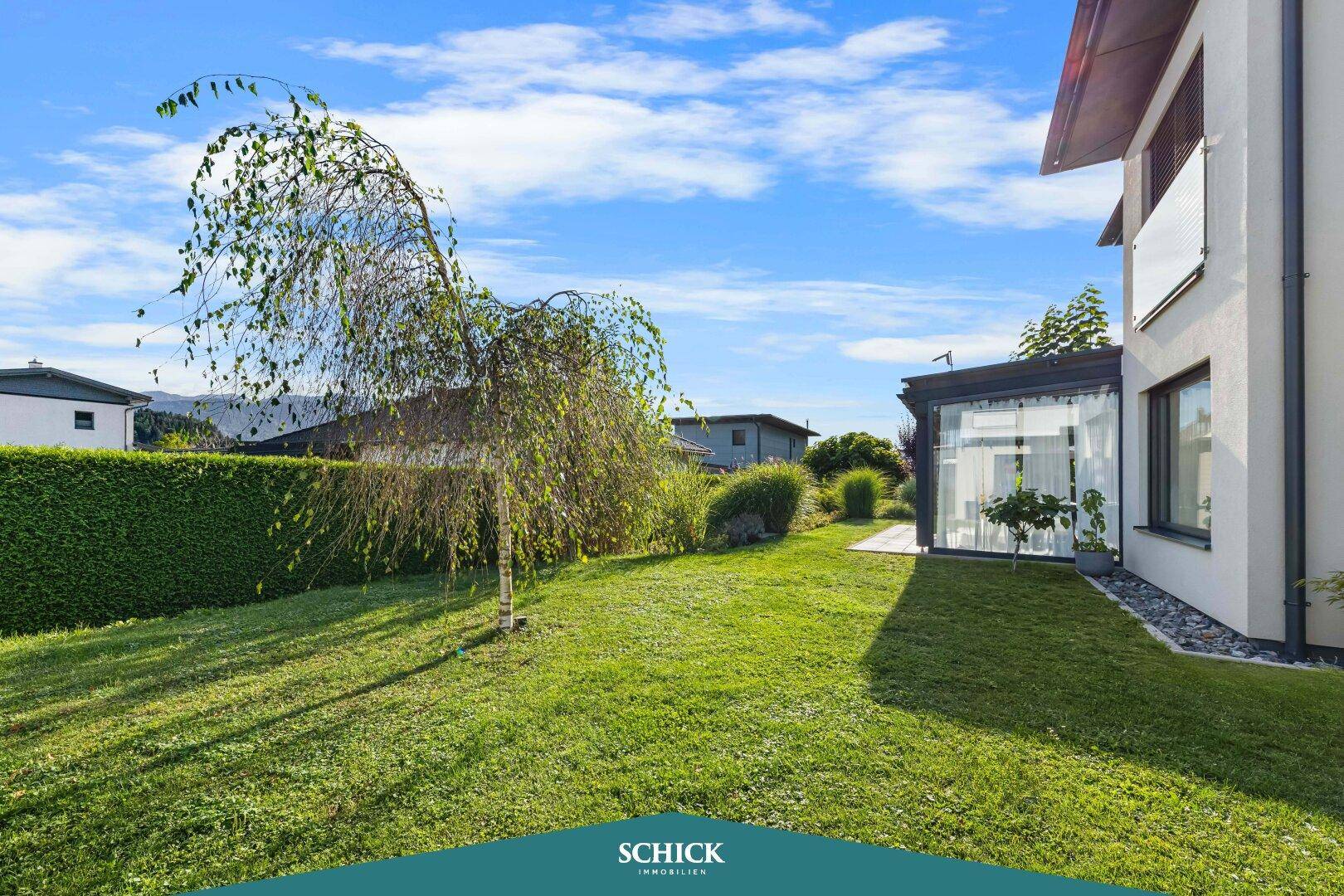 Gepflegter Gartenbereich mit Rasenfläche, einem jungen Baum und einer dichten Hecke neben dem Haus.