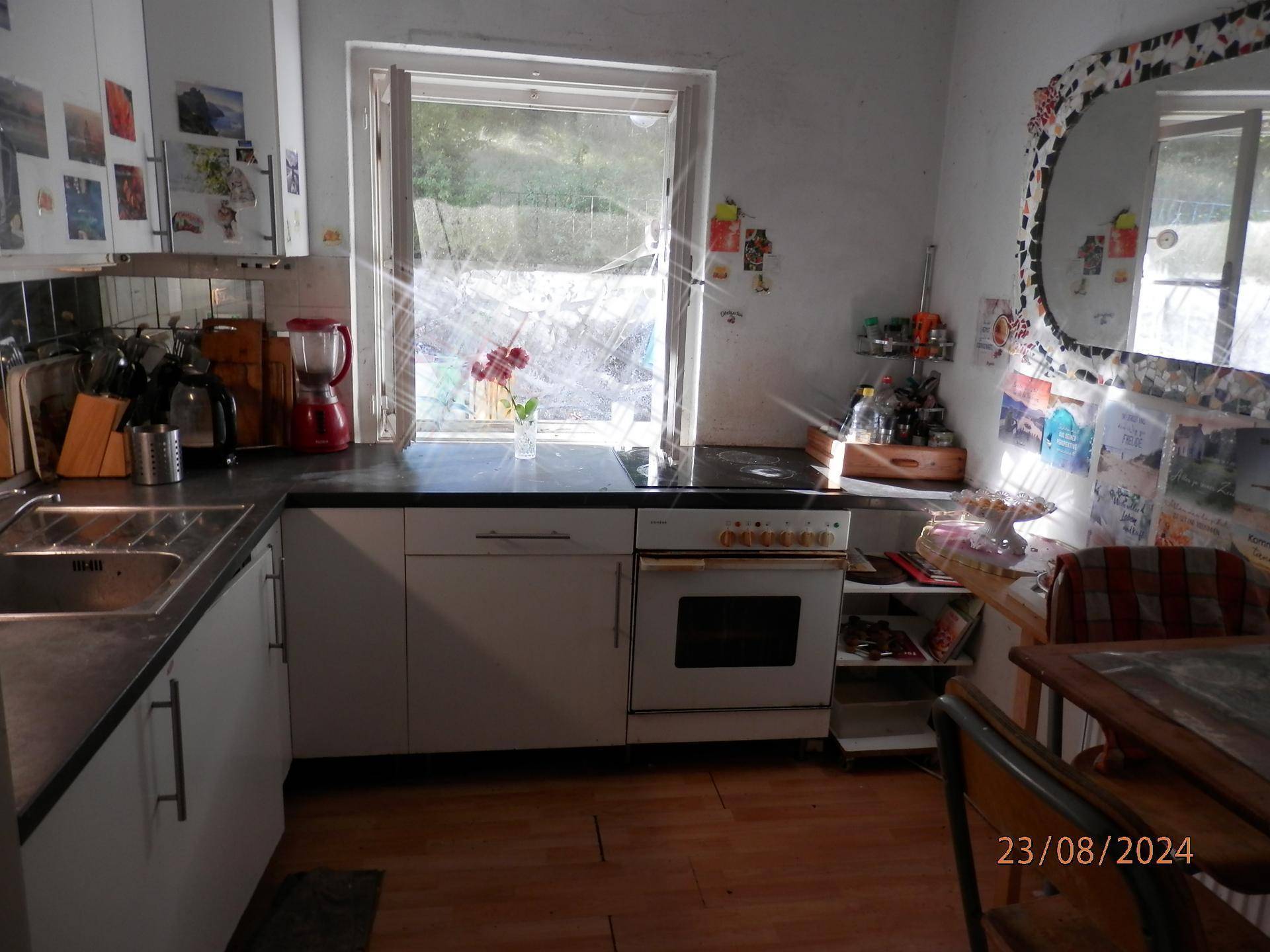Küche mit weißen Schränken, Herd und Spüle, hell durch Fenster.