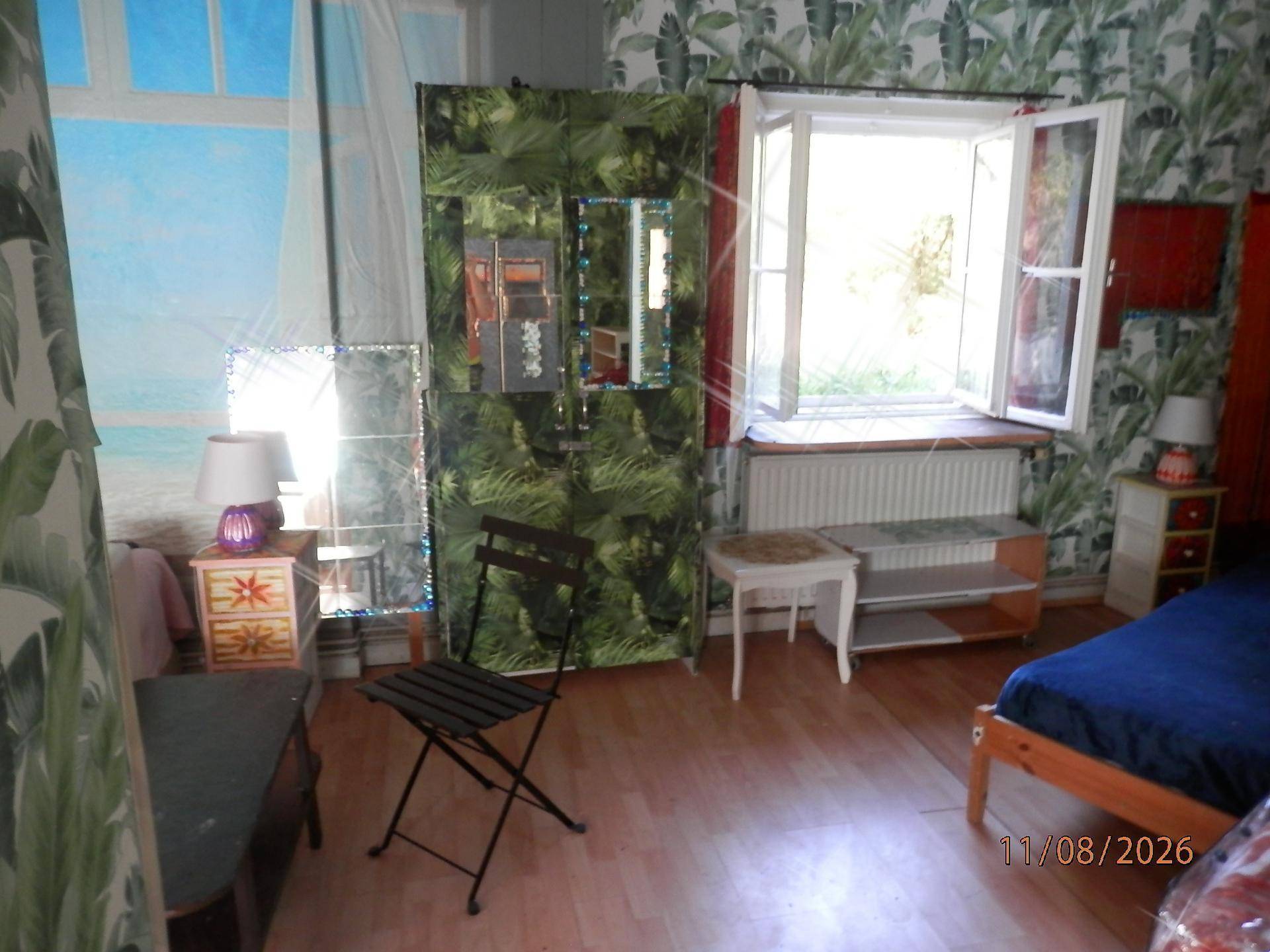 Schlafzimmer mit tropischer Tapete, Einzelbett und geöffnetem Fenster.