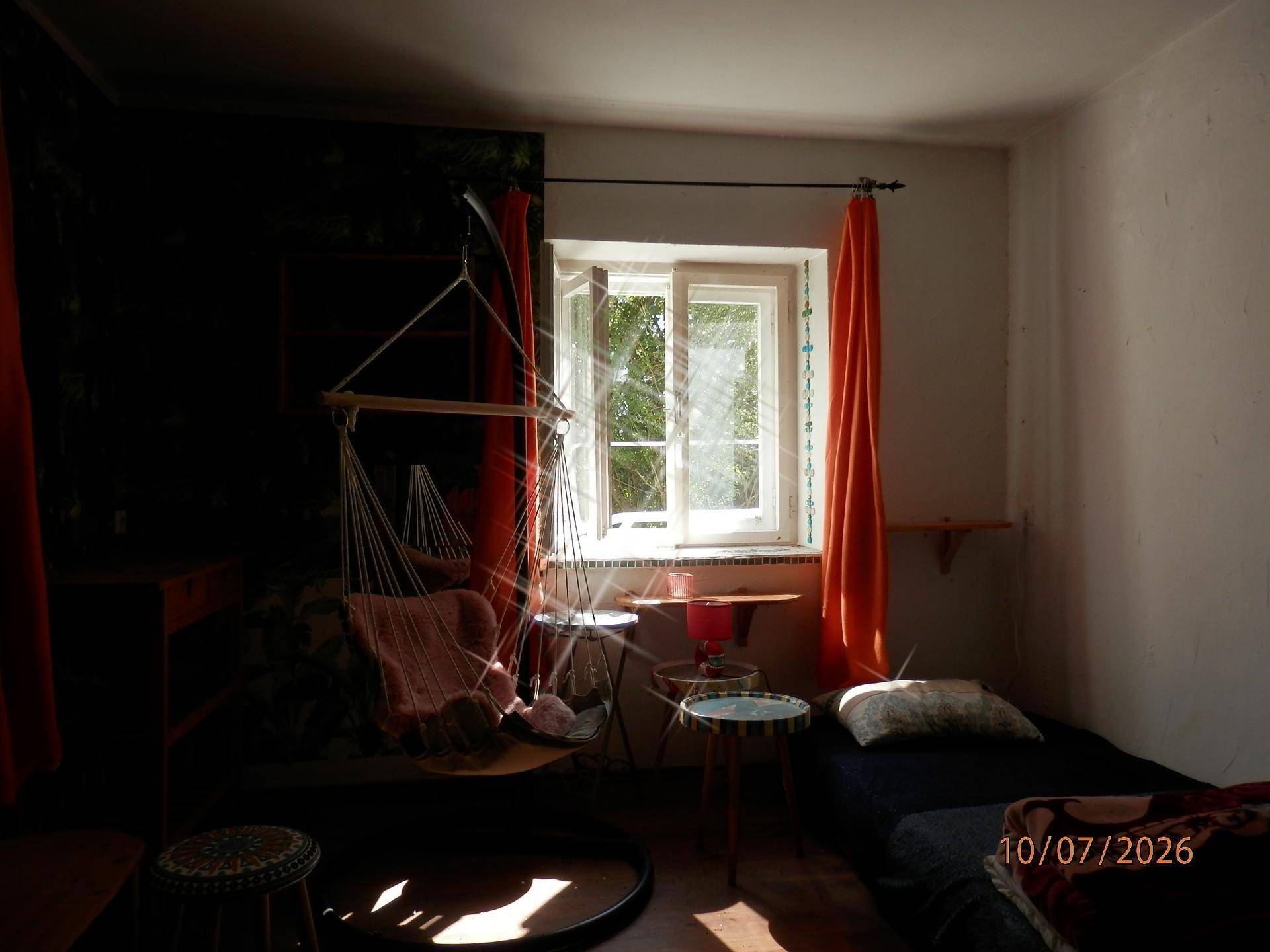 Schlafzimmer mit Einzelbett, Hängesessel und hellem Fenster.