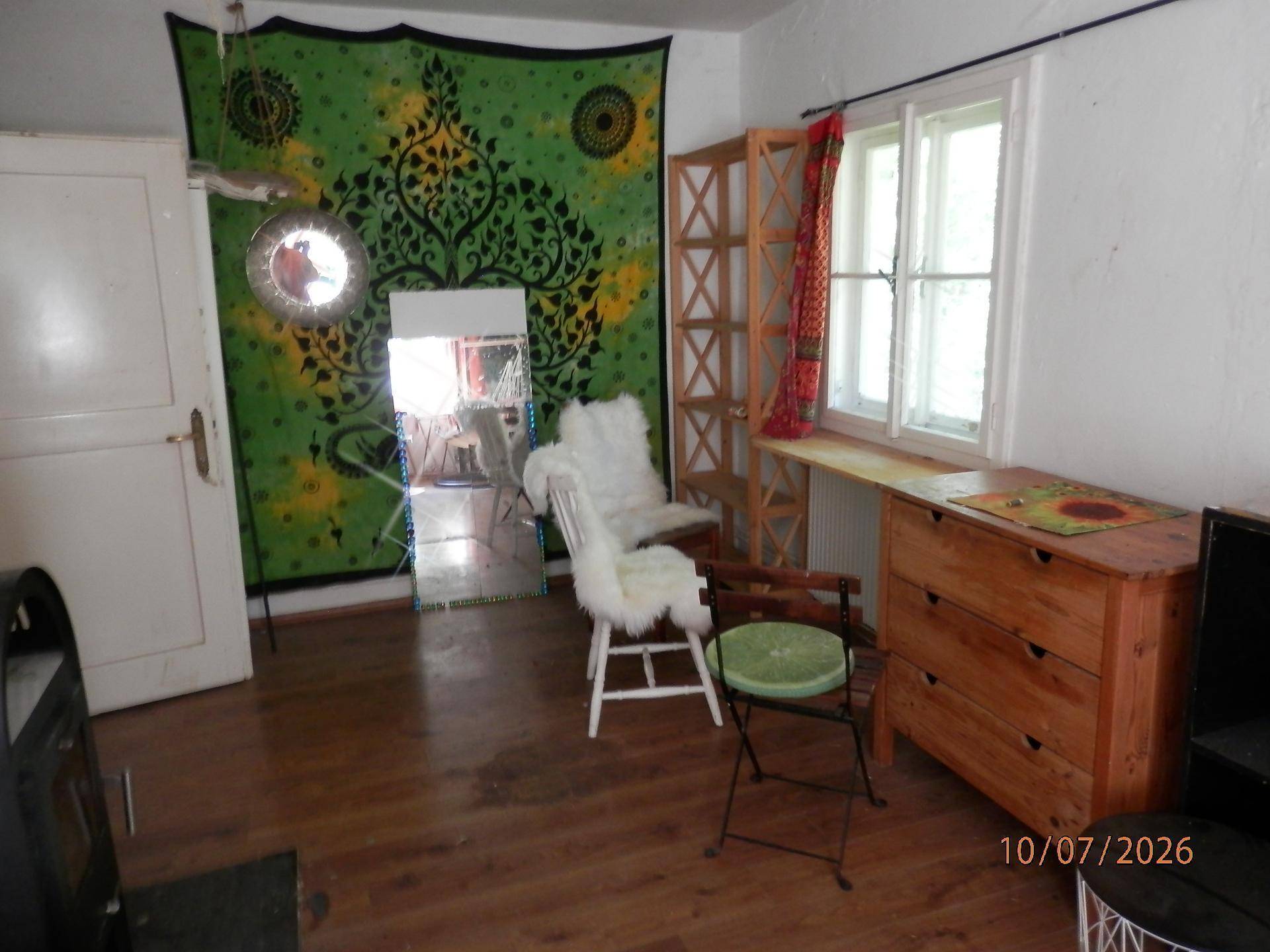 Wohnbereich mit Holzboden, Kommode und großem Spiegel an der Wand.