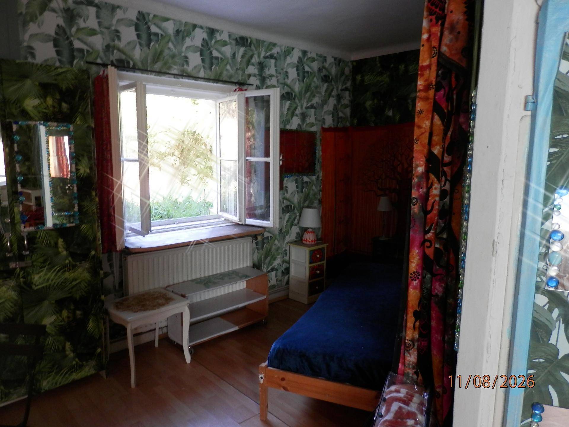 Schlafzimmer mit Einzelbett, tropischer Tapete und hellem Fenster.
