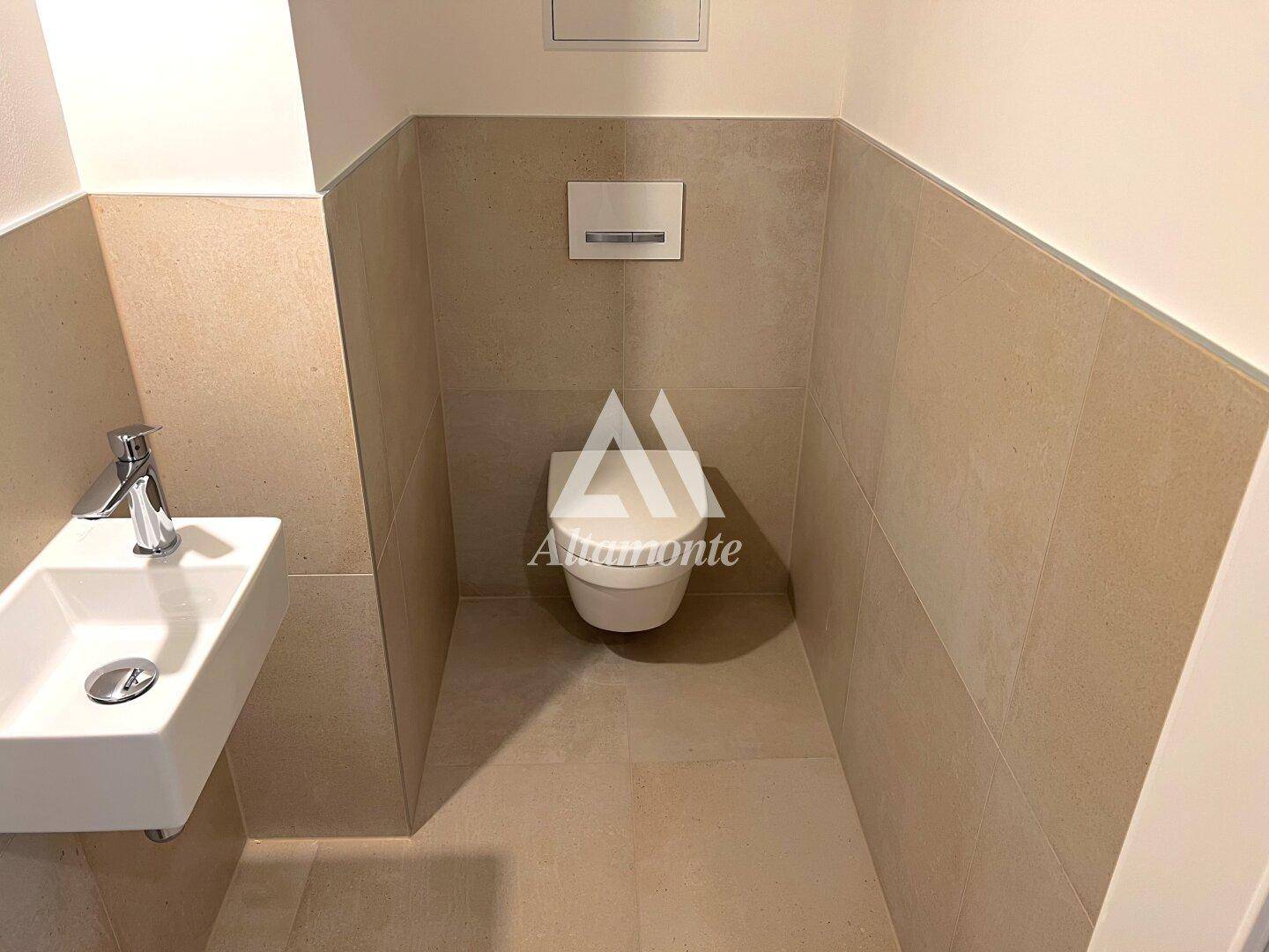 Kompaktes Gäste-WC mit wandhängender Toilette und kleinem Waschbecken, modern gefliest.