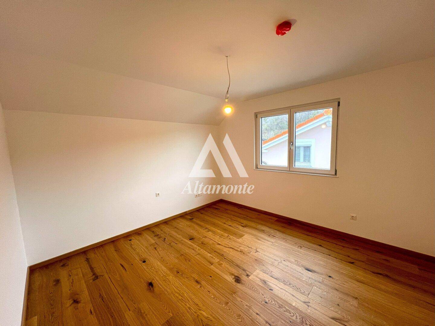 Helles Schlafzimmer mit Holzboden und Fenster, das viel Tageslicht hereinlässt.