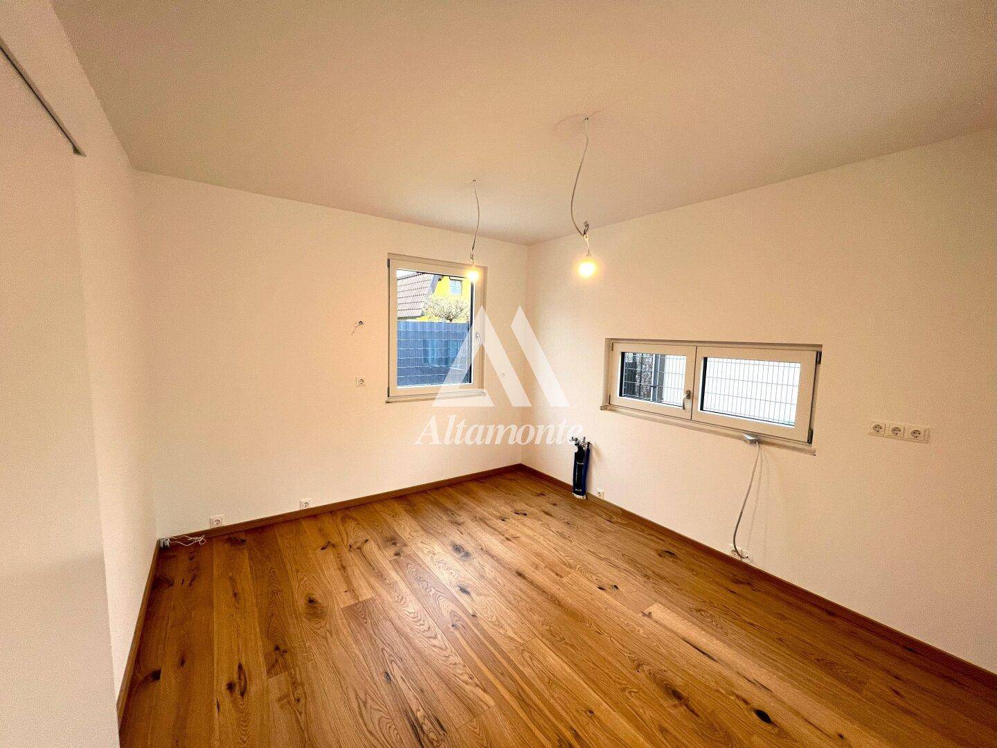 Leeres Zimmer mit Holzboden und zwei Fenstern, bereit für die individuelle Gestaltung.