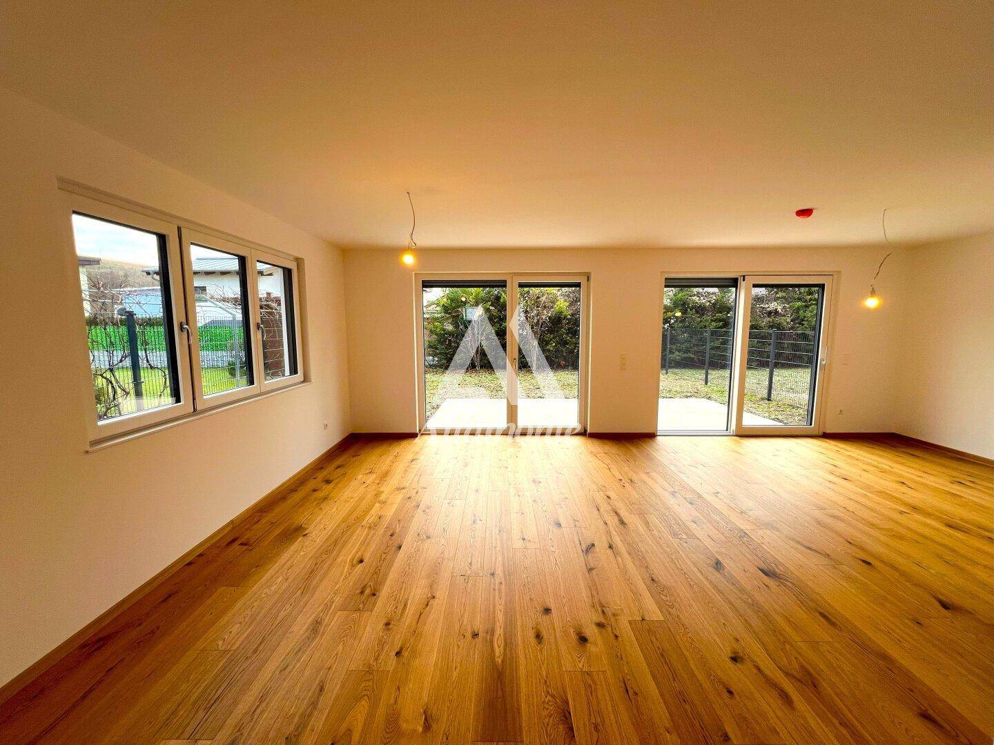 Heller Wohnraum mit Holzboden und großen Terrassentüren, die Zugang zum Garten bieten.