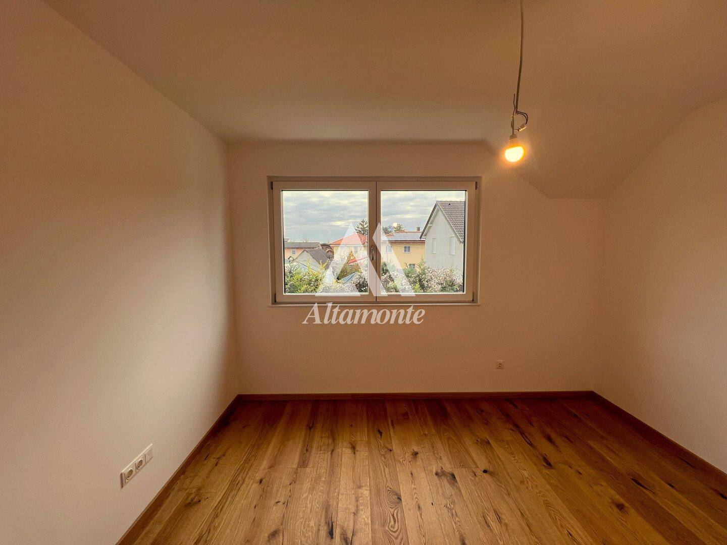 Geräumiges Zimmer mit Holzboden und großem Fenster, das einen Blick nach draußen bietet.
