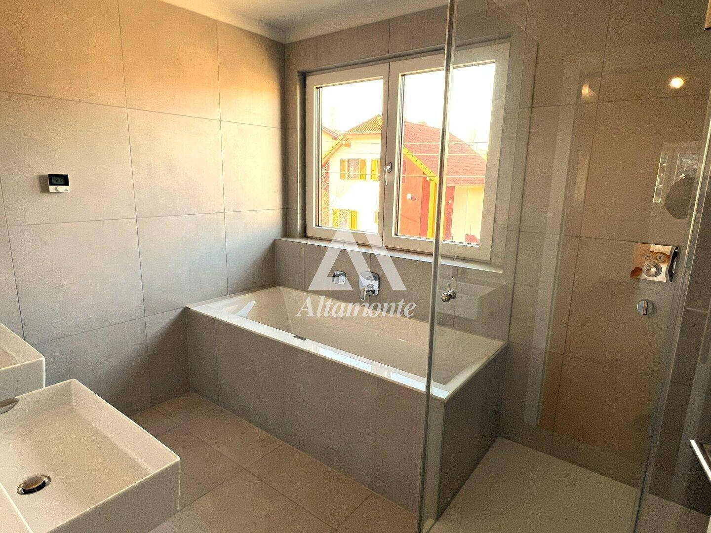 Modernes Badezimmer mit grauen Fliesen, Badewanne, begehbarer Dusche und Doppelwaschbecken.