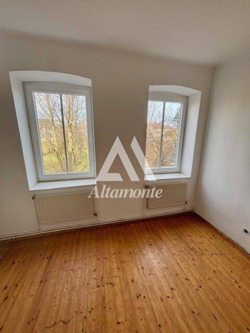 Helles Schlafzimmer mit Holzboden und zwei Fenstern, die viel Tageslicht hereinlassen.