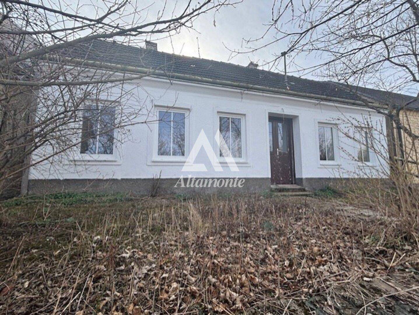 Vorderansicht eines einfachen Landhauses mit weißer Fassade und brauner Eingangstür.