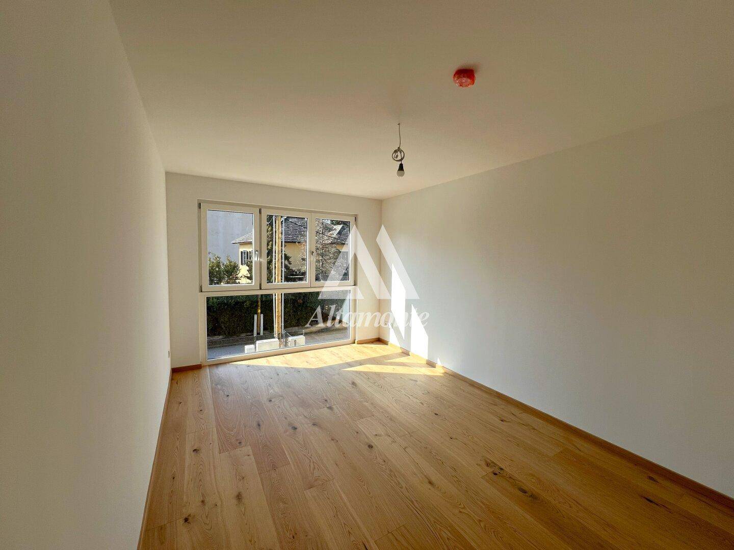 Freundliches Zimmer mit Holzboden und breitem Fenster, das eine angenehme Atmosphäre schafft.