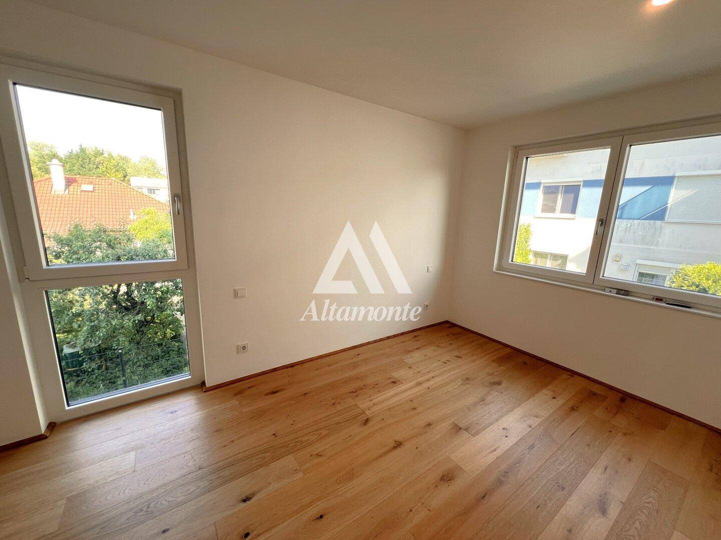 Helles Schlafzimmer mit Holzboden und zwei Fenstern, die viel Tageslicht hereinlassen.