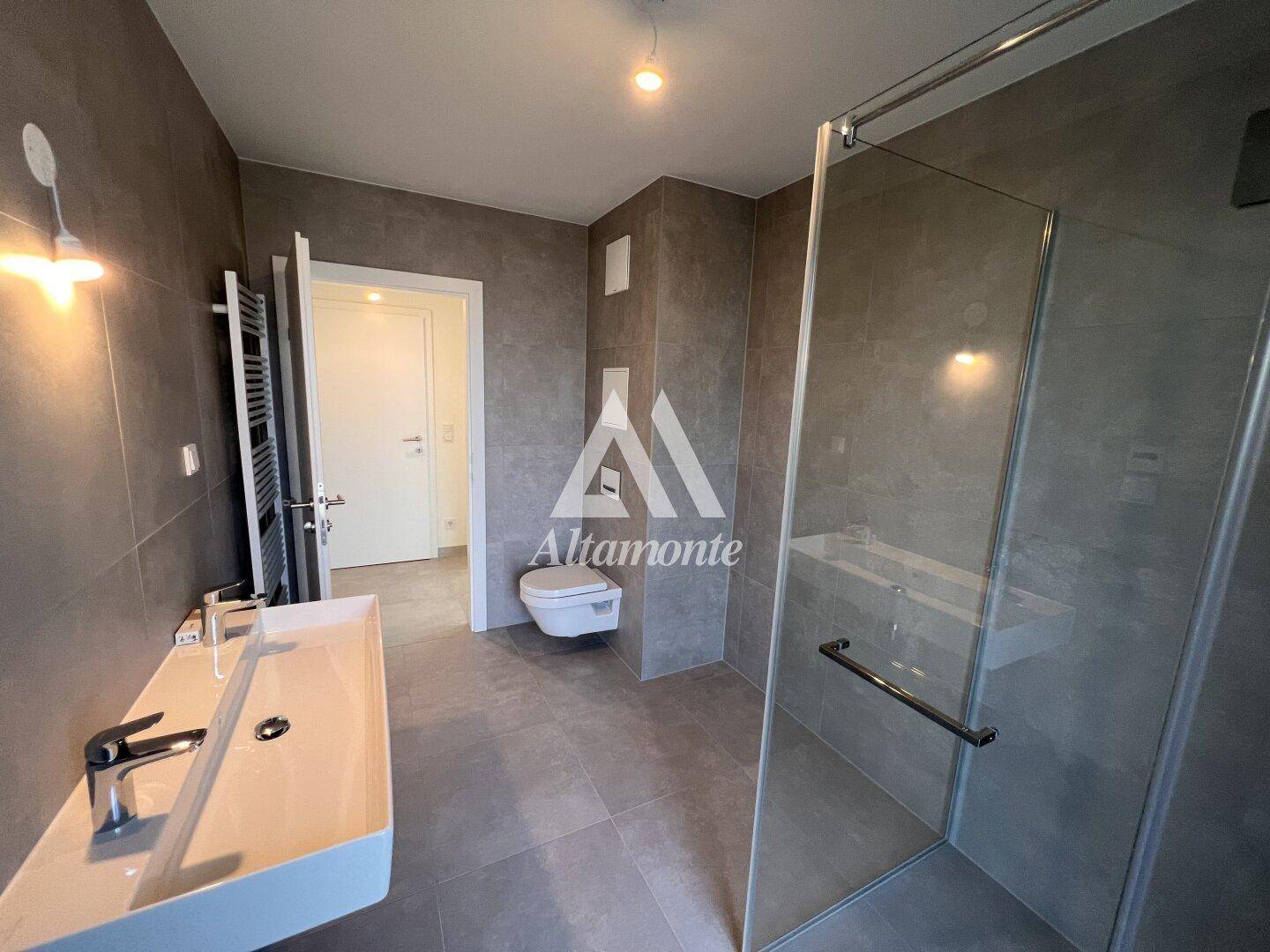 Modernes Badezimmer mit grauen Fliesen, begehbarer Dusche und wandhängendem WC.