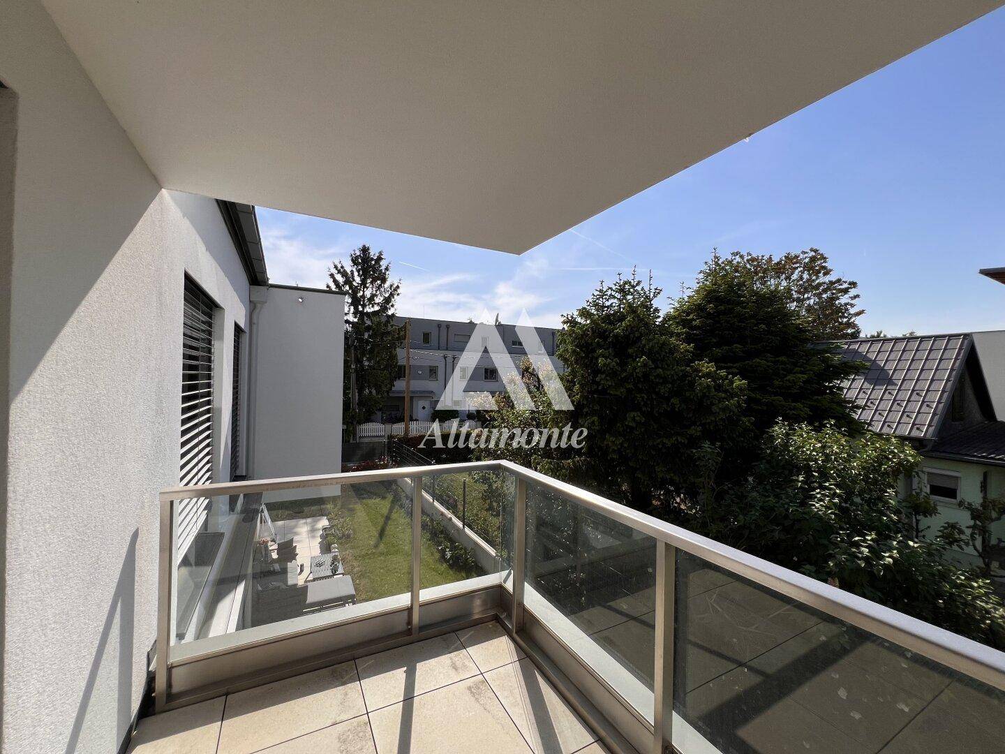 Kleiner Balkon mit Glasgeländer und Blick auf den Gartenbereich und benachbarte Gebäude.