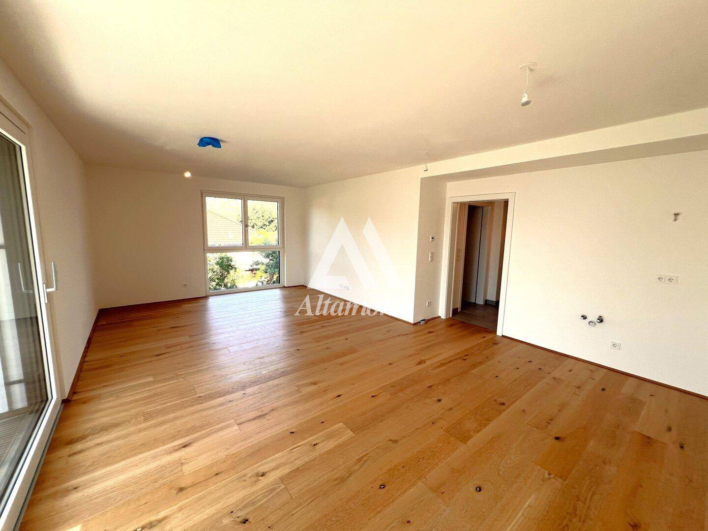 Geräumiges Wohnzimmer mit Holzboden und großen Fenstern, bereit für die Einrichtung.
