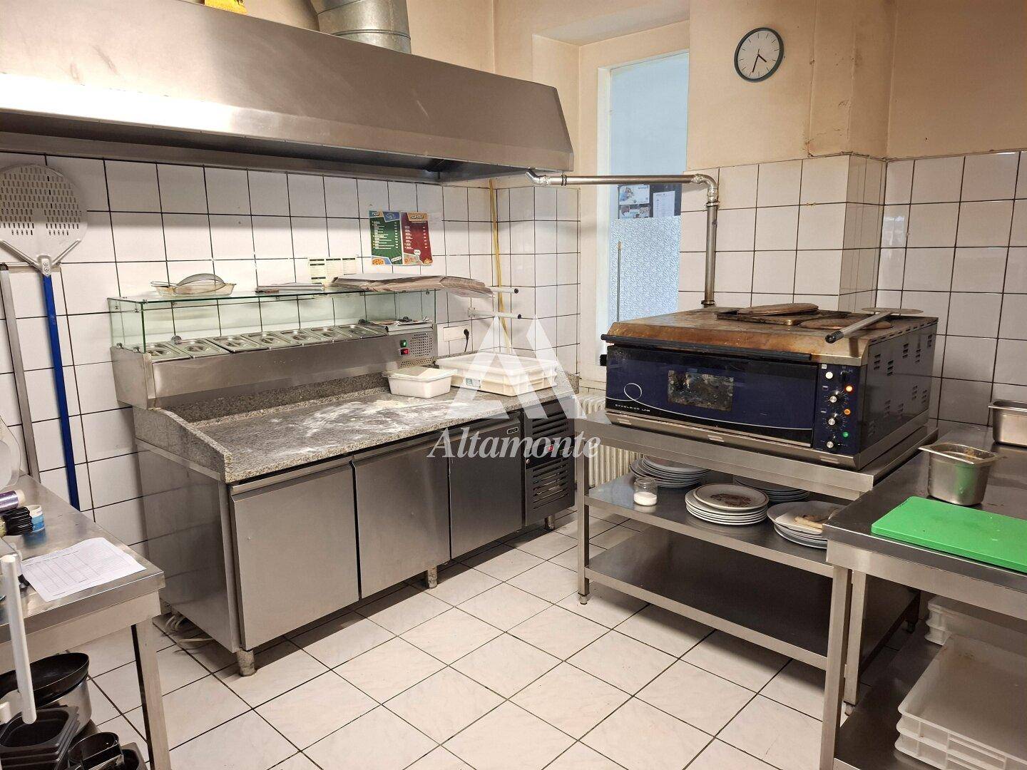 Professionelle Gewerbeküche mit Edelstahlgeräten, Fliesenwänden und einem großen Pizzaofen.