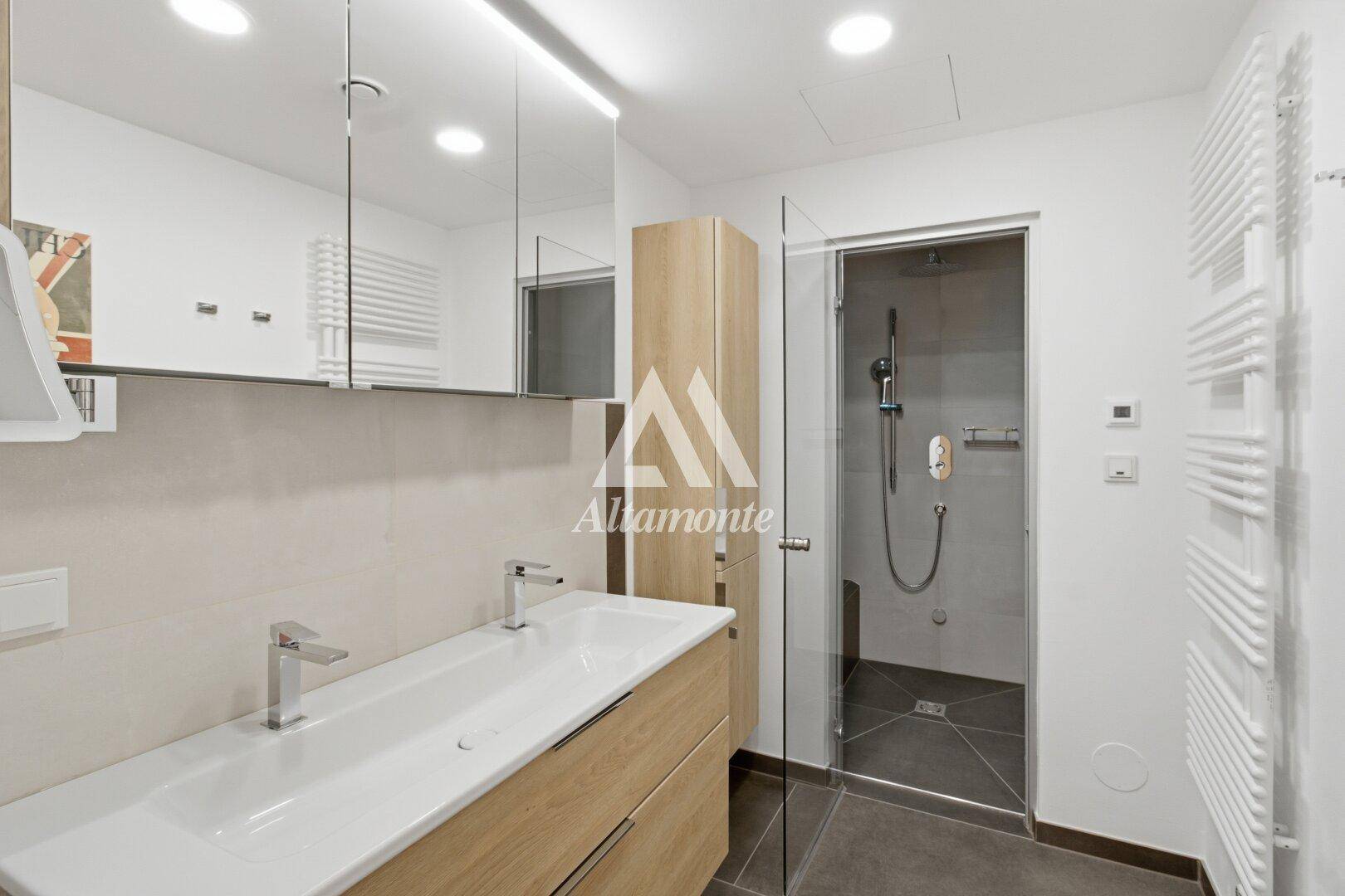 Modernes Badezimmer mit Doppelwaschbecken, großer begehbarer Dusche und Handtuchheizkörpern.