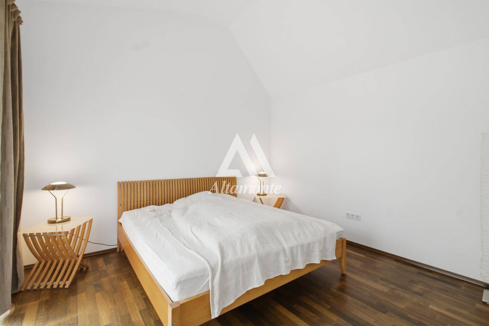 Gemütliches Schlafzimmer mit Holzbett, Holzboden und schrägen Wänden unter dem Dach.