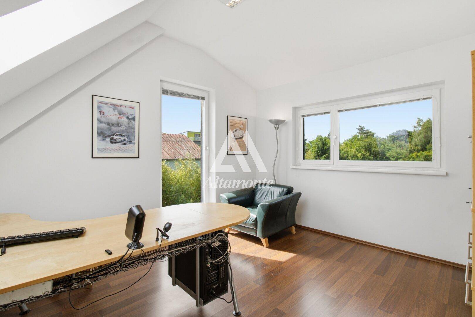 Helles Arbeitszimmer mit Holzboden, Schreibtisch und Blick ins Grüne durch die Fenster.