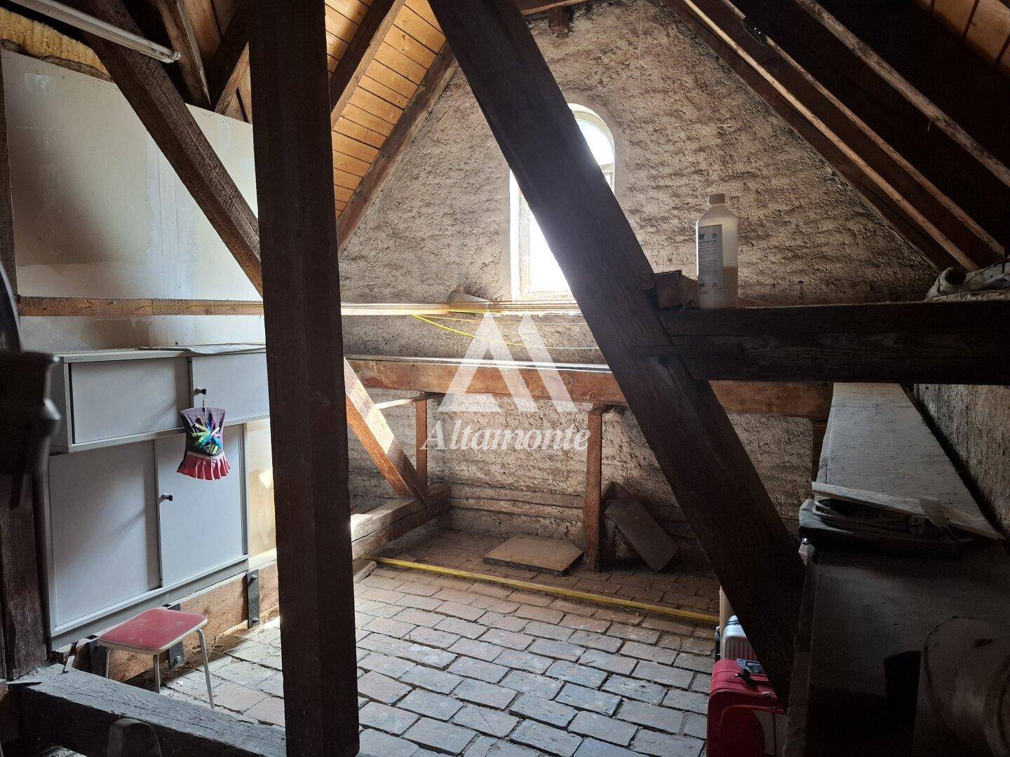 Rustikaler Dachboden mit sichtbaren Holzbalken, Ziegelboden und kleinem Fenster, ideal als Stauraum.
