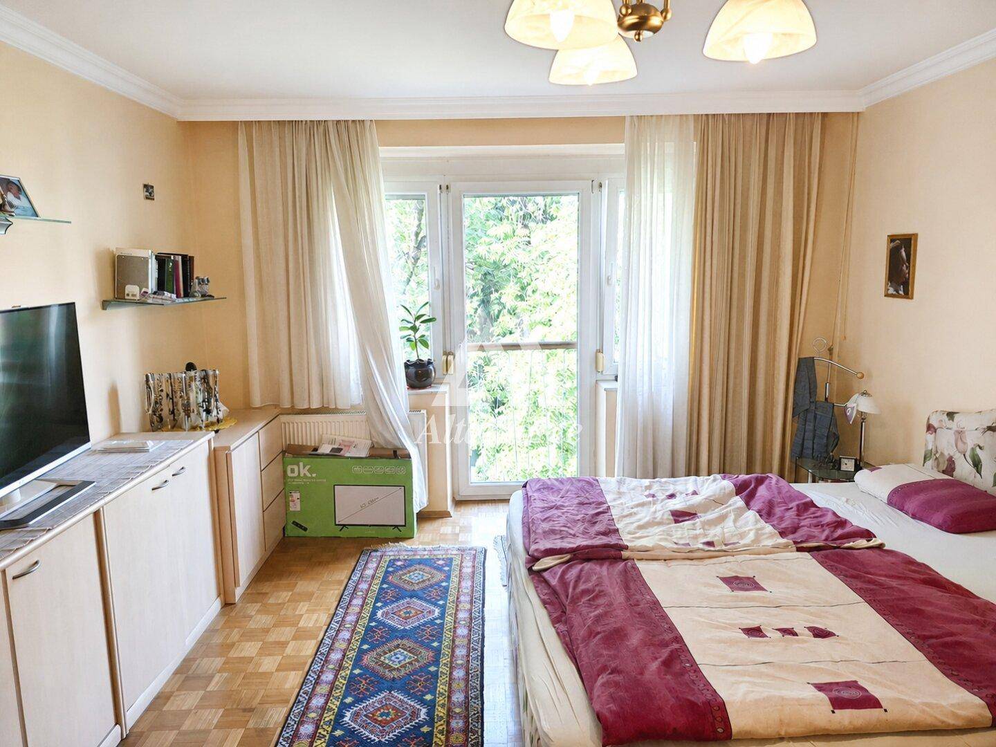 Gemütliches Schlafzimmer mit Bett, TV-Möbeln und großem Fenster mit Blick ins Grüne.