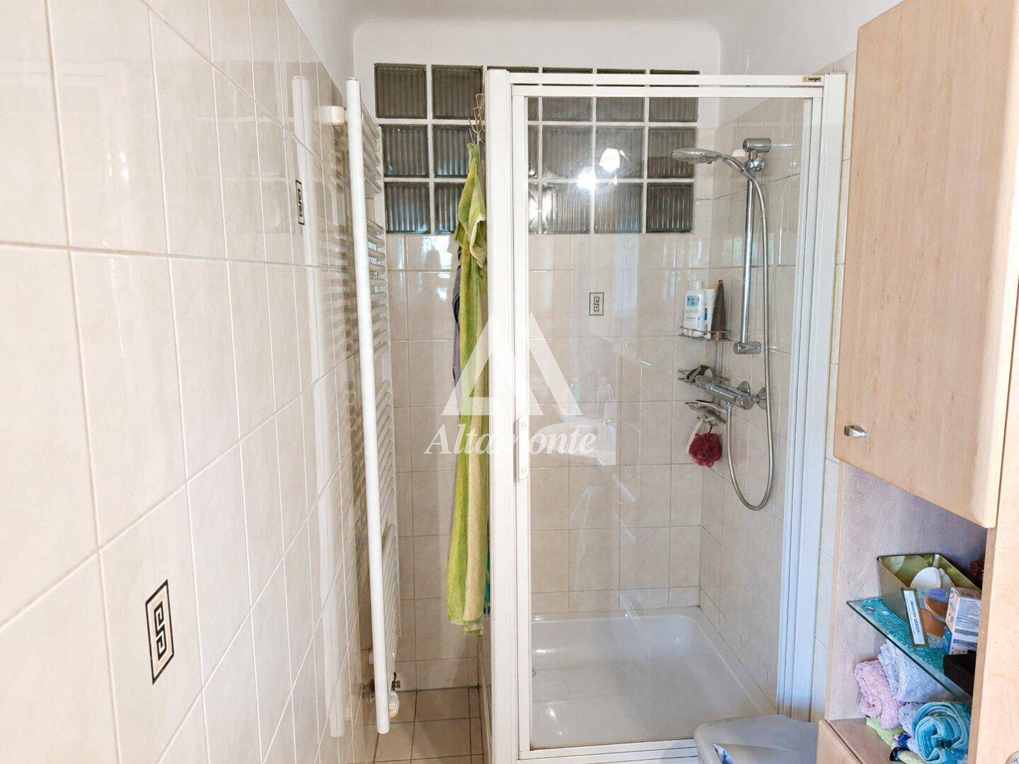 Helles Badezimmer mit Duschkabine, Fliesenwänden und einem praktischen Handtuchheizkörper.