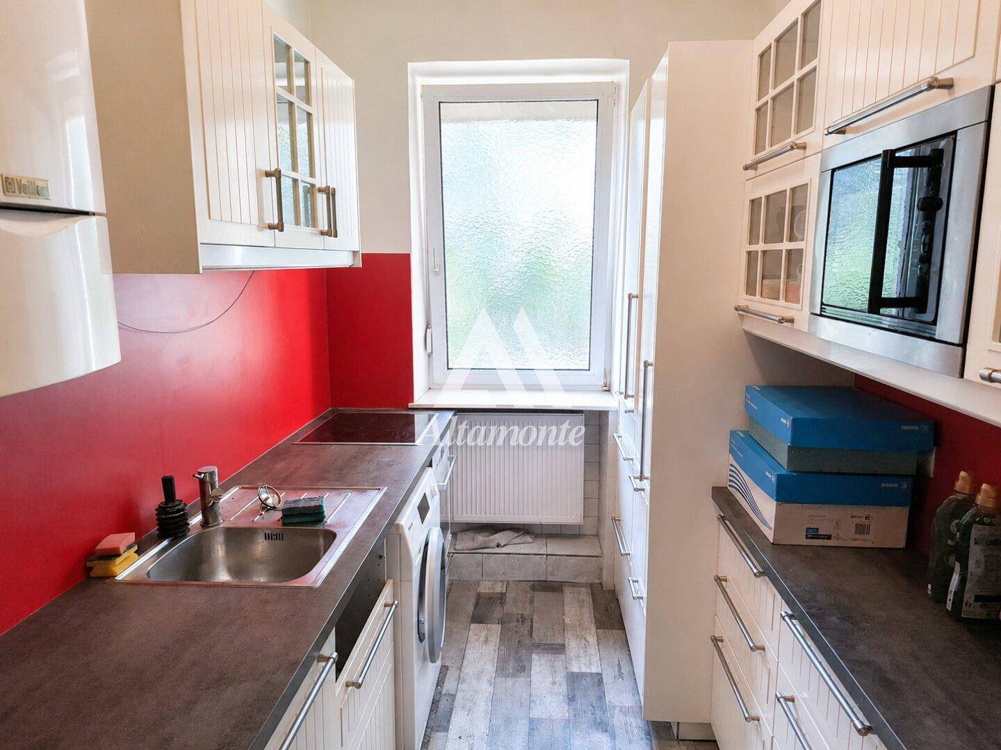 Moderne Küche mit weißen Schränken, roter Rückwand, Induktionskochfeld und integrierter Mikrowelle.