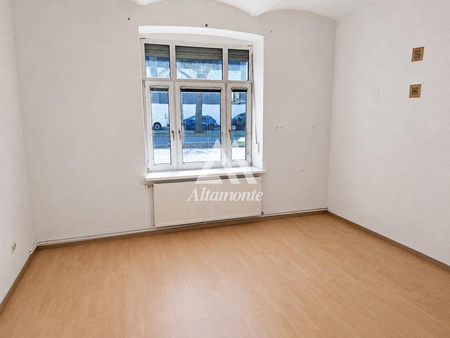 Leerer Raum mit weißen Wänden, Laminatboden und großem Fenster zur Straße.