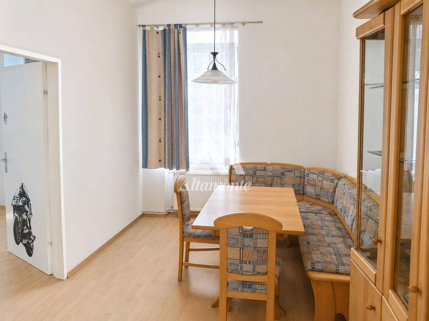 Gemütlicher Essbereich mit Eckbank, Holztisch und einem Vitrinenschrank neben dem Fenster.