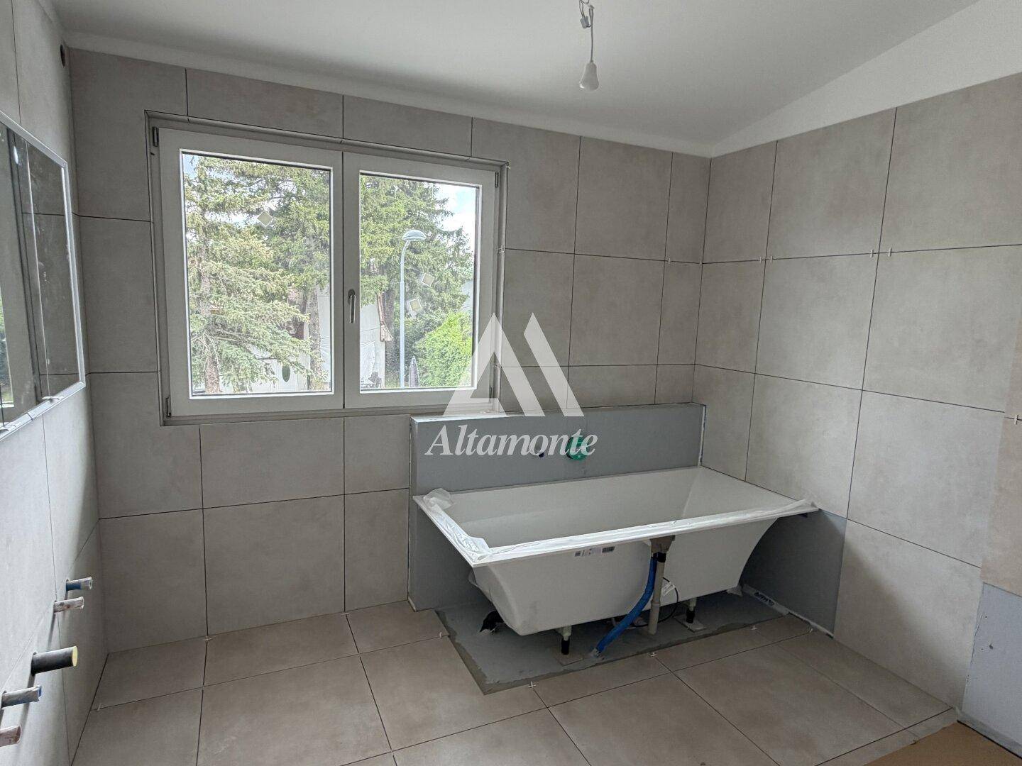 Badezimmer im Rohbau mit Fliesenboden, großen Fenstern und einer freistehenden Badewanne.