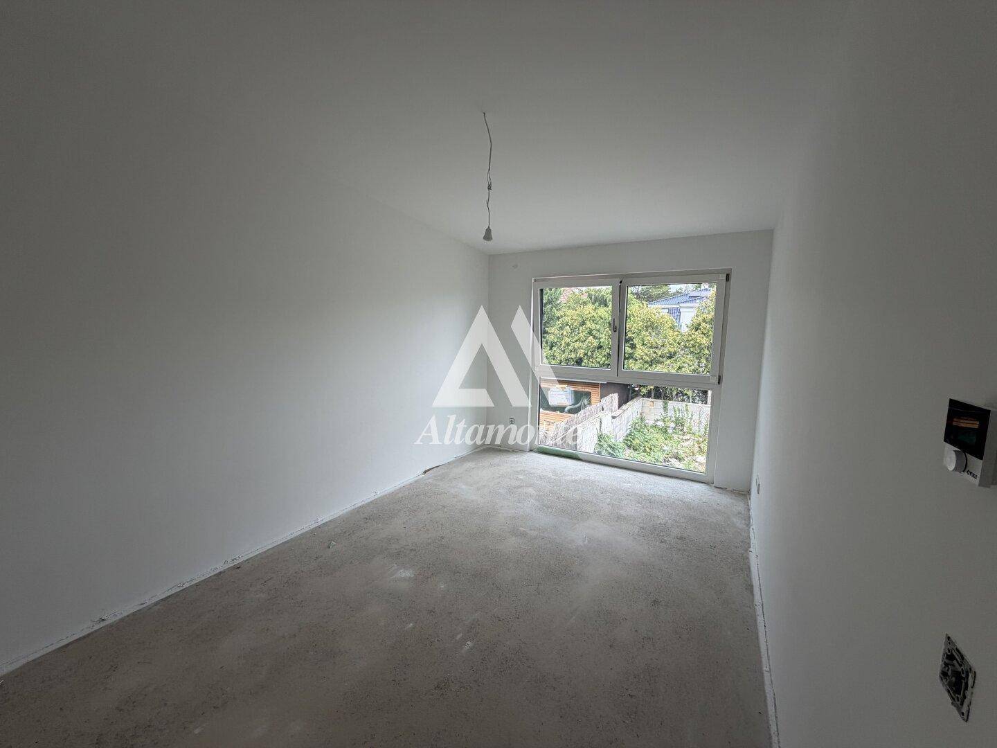 Weiteres helles Zimmer im Rohbau mit großem Fenster und Blick ins Grüne.