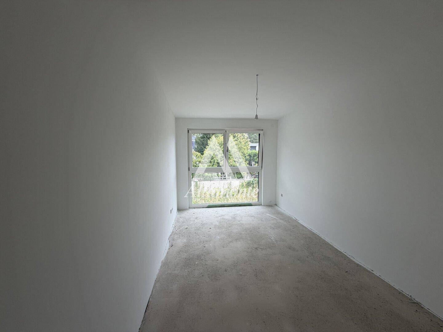 Unfertiges Zimmer mit großen Fenstern, die viel Licht hereinlassen und eine grüne Aussicht bieten.
