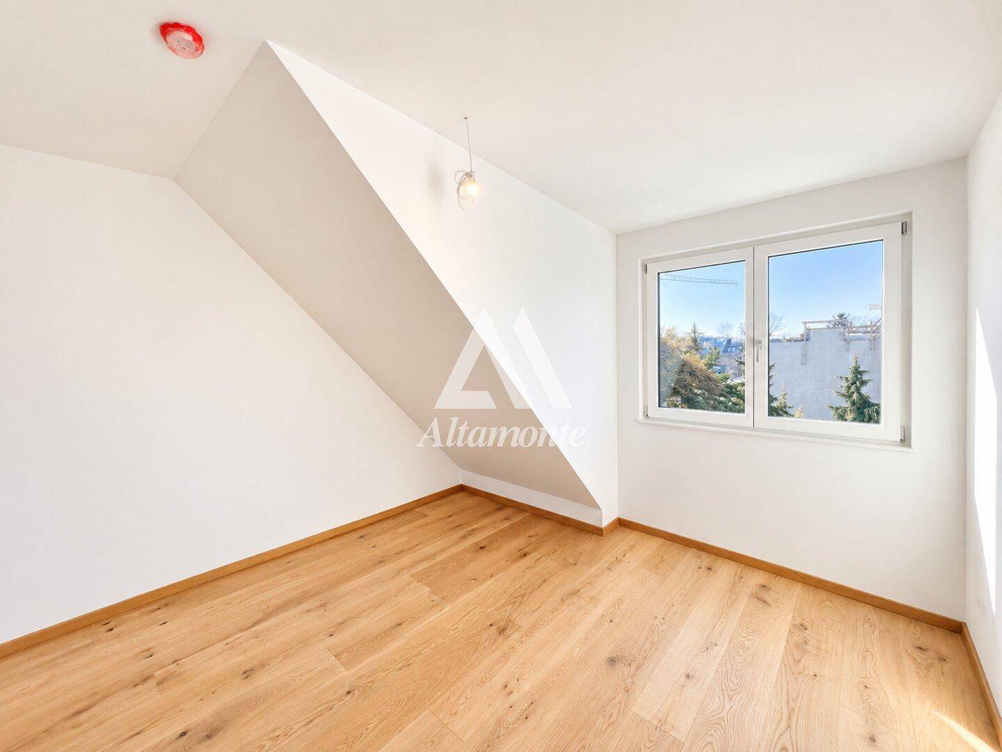 Dachgeschosszimmer mit Holzboden, schräger Decke und Fenster mit Blick auf die Umgebung.