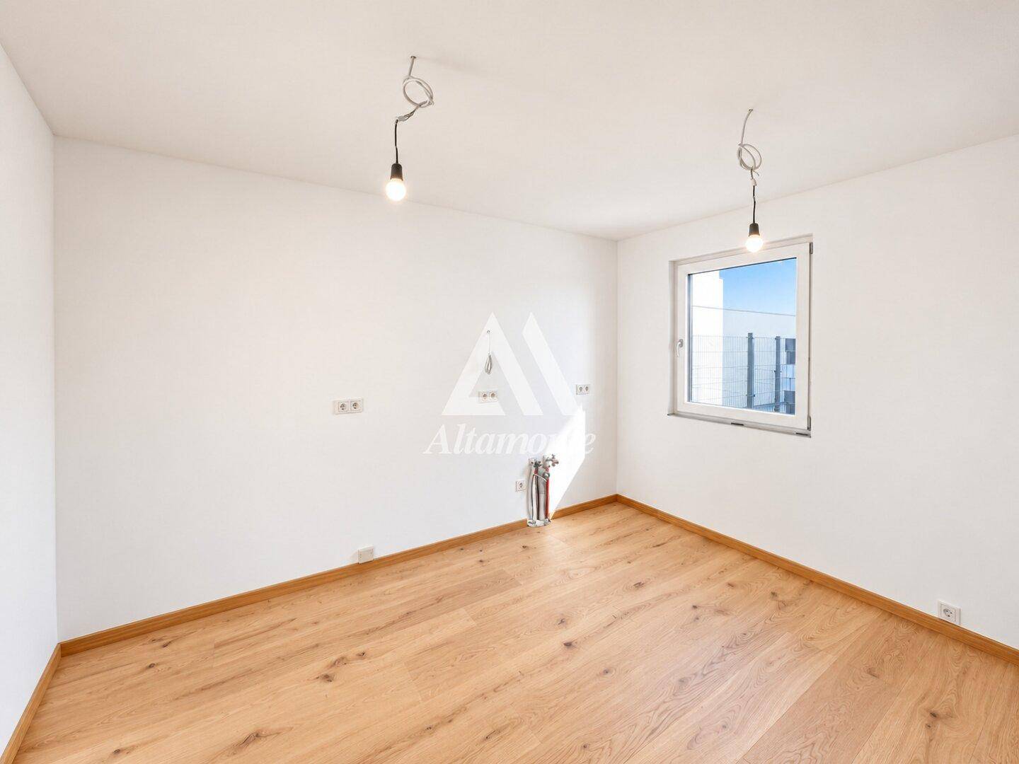 Helles Zimmer mit Holzboden und großem Fenster, ideal als Schlaf- oder Arbeitszimmer nutzbar.