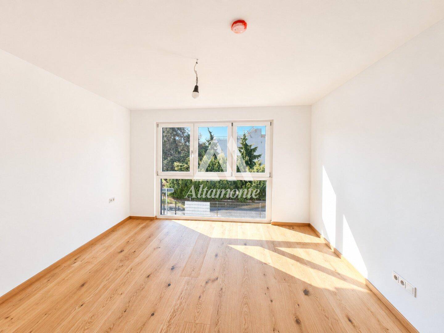 Geräumiges Schlafzimmer mit Holzboden und großem Fenster, das viel natürliches Licht hereinlässt.