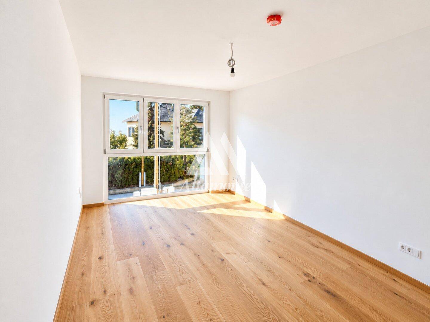 Helles Schlafzimmer mit Eichenparkett und breitem Fenster, das einen Blick ins Grüne bietet.