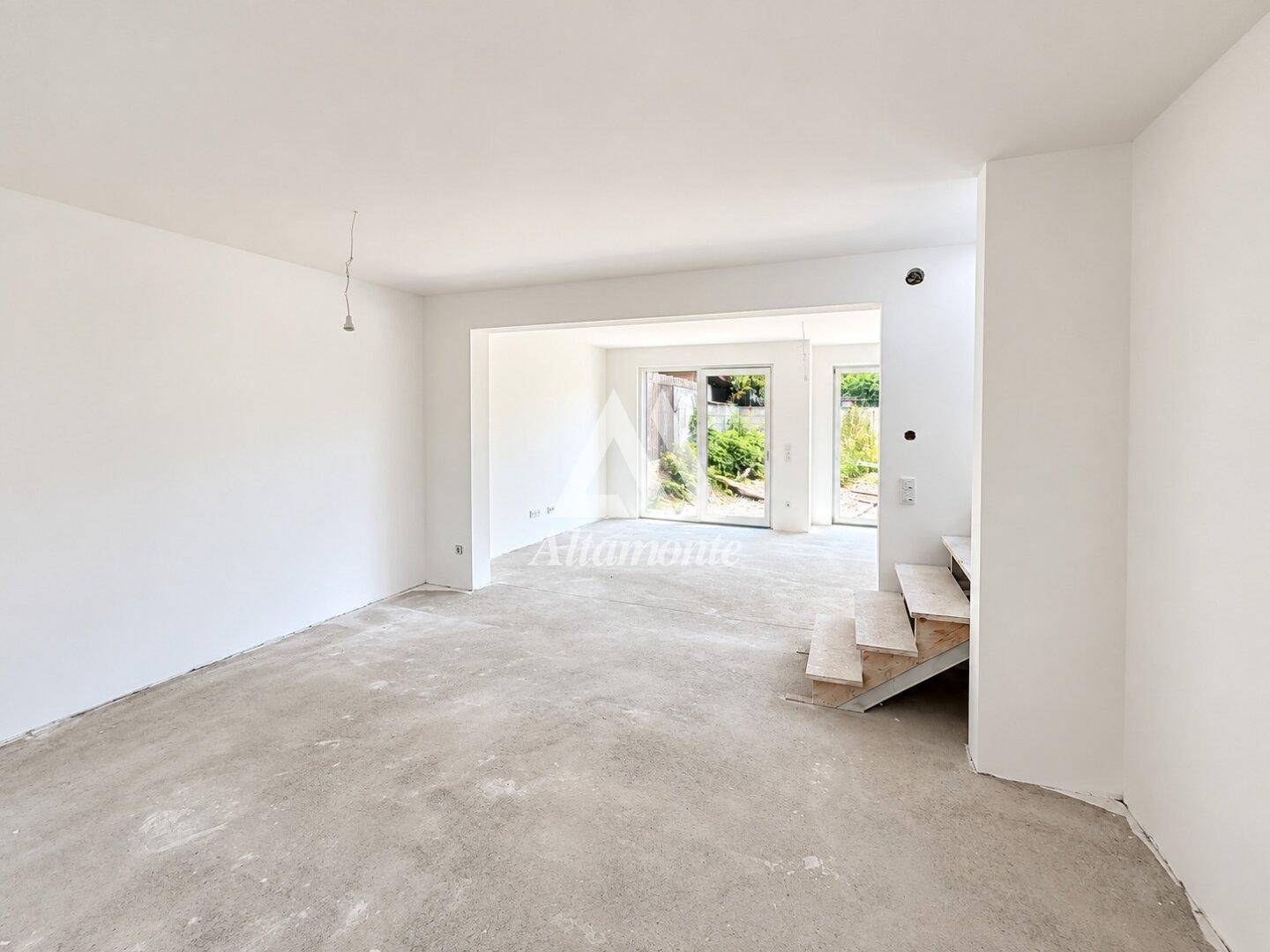 Unmöblierter Wohnbereich im Rohbau mit Betonboden und großen Fenstern, viel Potenzial.