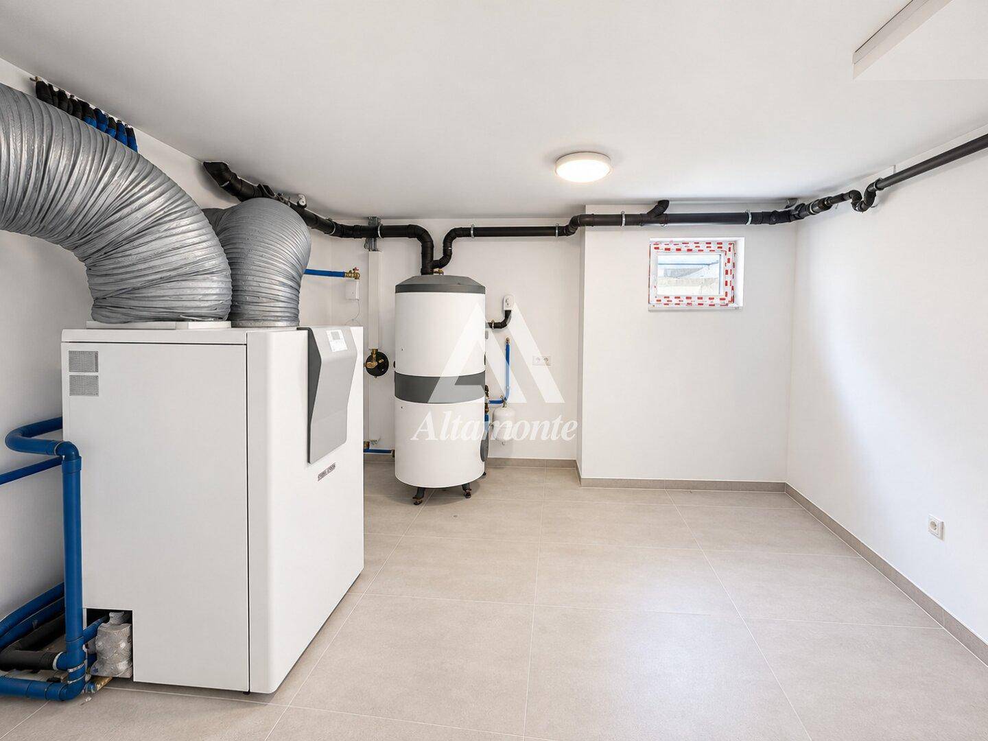 Heller Hauswirtschaftsraum mit moderner Wärmepumpe, Warmwasserspeicher und kleinem Fenster.