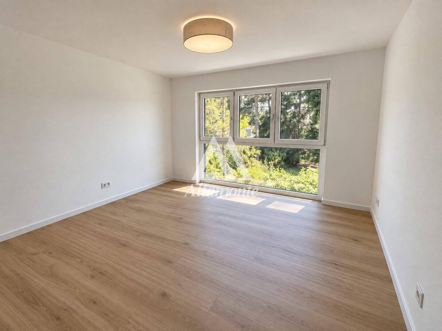 Helles, unmöbliertes Schlafzimmer mit Holzboden und großem Fenster mit Blick ins Grüne.