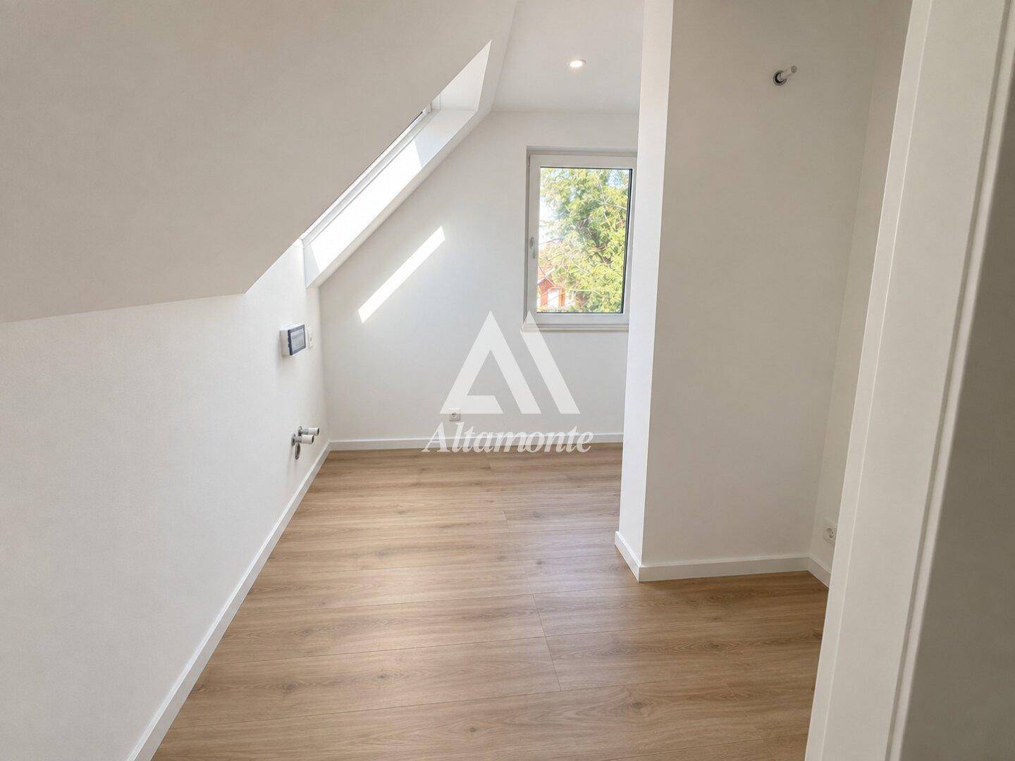 Dachgeschosszimmer mit schräger Decke, Holzboden und Dachfenster für viel Tageslicht.