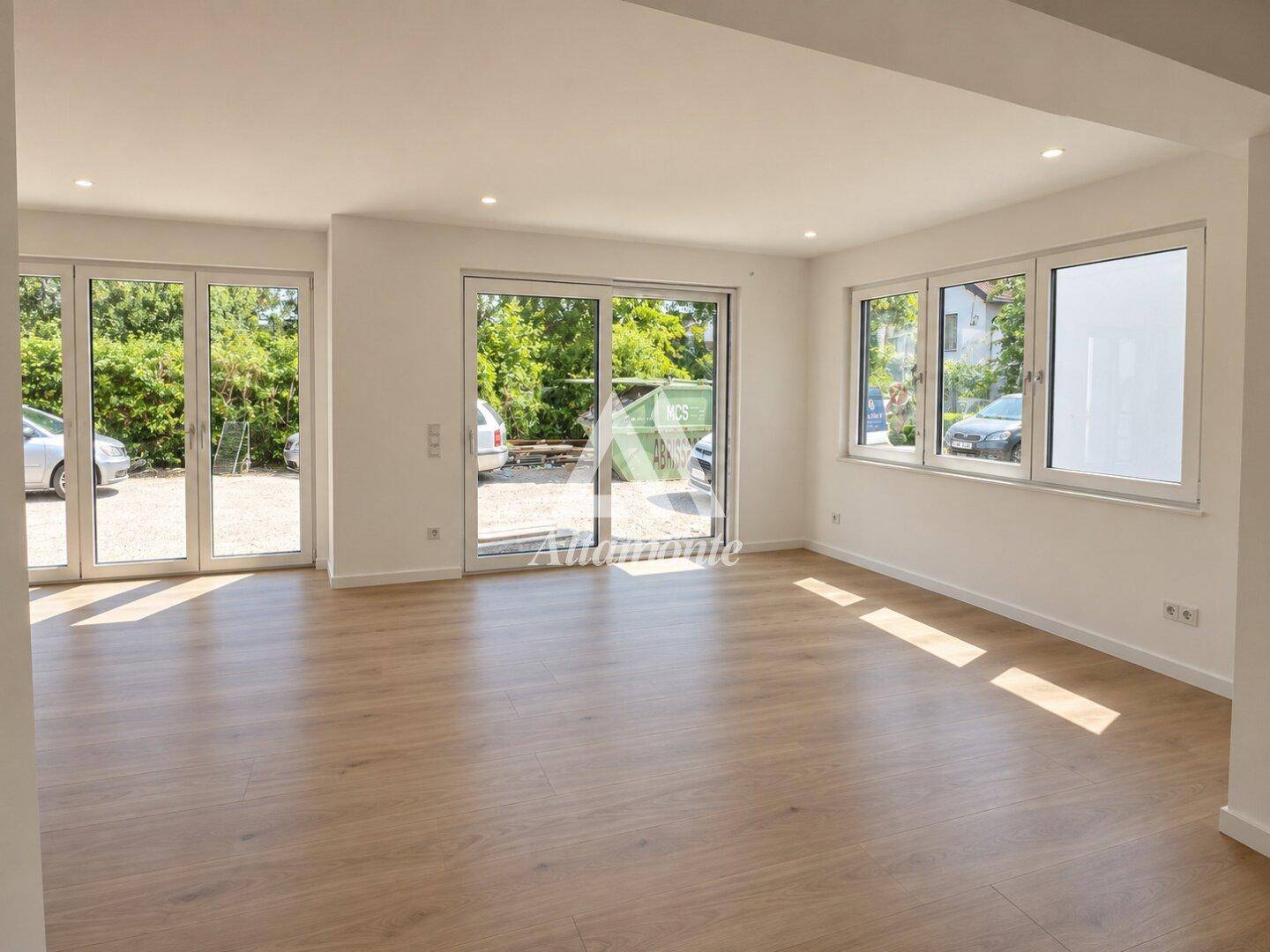 Geräumiges, unmöbliertes Wohnzimmer mit großen Fenstern und direktem Zugang zum Außenbereich.